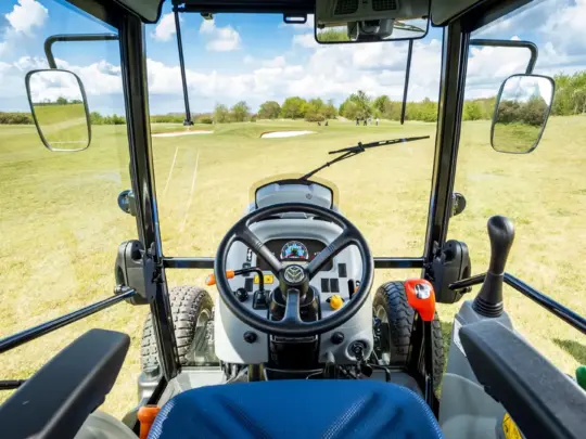 Førerhusvisning av en mini traktor Boomer 25 C-55 som ser ut over en golfbane.