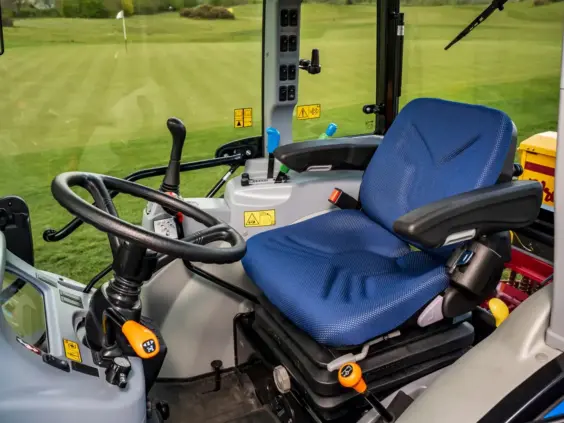 Interiøret i en Boomer 25 C-55 mini traktor med blått sete og utsikt over golfbane.