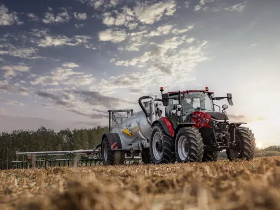 Case IH Farmall med gjødselvogn og stripespreder i solnedgang