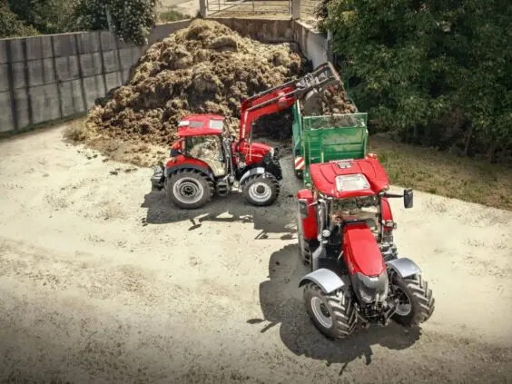 Rød traktor fra Vestrum-serien laster materiale i en grønn tilhenger på en gård.
