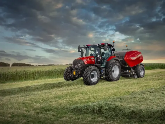 Rød traktor fra Vestrum-serien med rundballepresse i en åker under en dramatisk himmel.