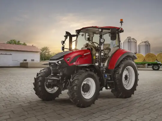 Rød Case traktor parkert på en gårdsplass med siloer i bakgrunnen.