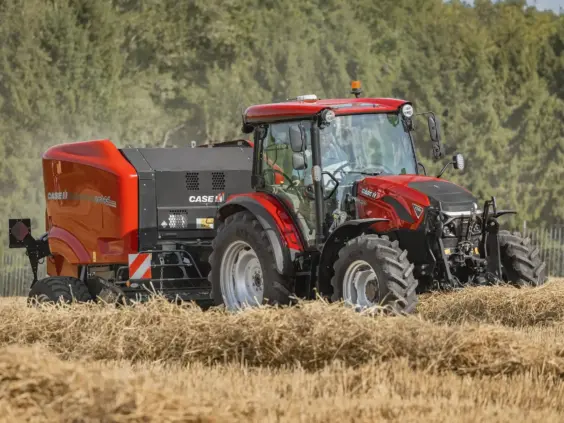 En rød Case IH-traktor som trekker en ballepresse på et jorde med halm.