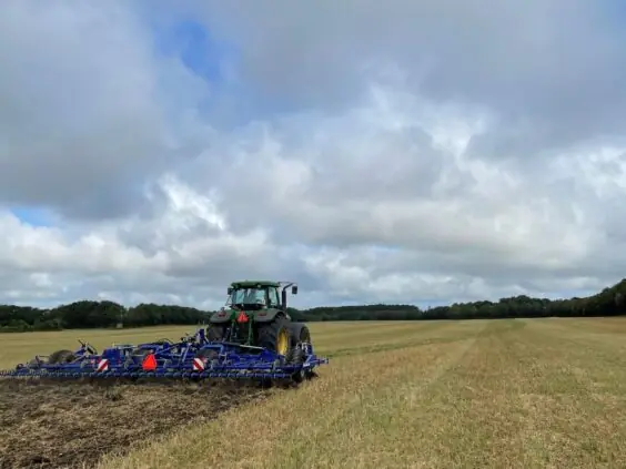 En grønn traktor som trekker en DALBO Cultimax Eco harv på en åker.