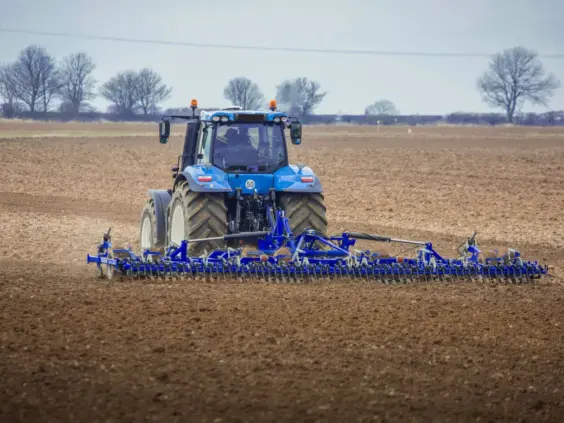 Blå traktor som trekker en DALBO Cultimax såbedsharv over et brunt jorde.