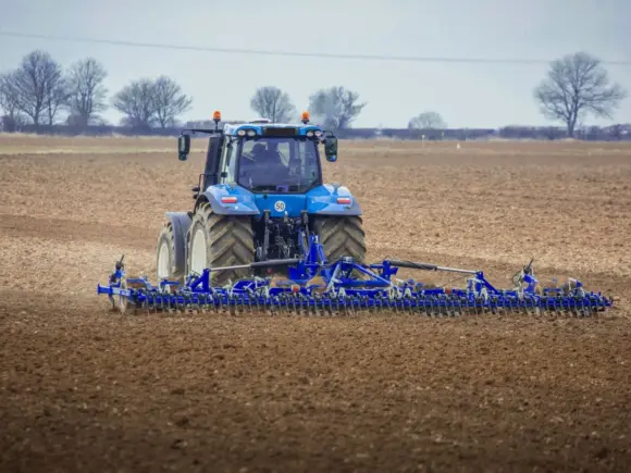 Blå traktor som trekker en DALBO Cultimax såbedsharv over et brunt jorde.