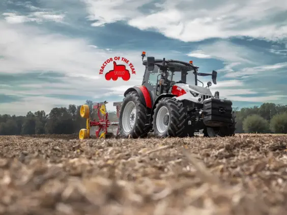En moderne Steyr Plus traktor som pløyer en åker under en dramatisk skyhimmel.