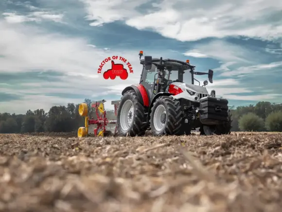En moderne Steyr Plus traktor som pløyer en åker under en dramatisk skyhimmel.