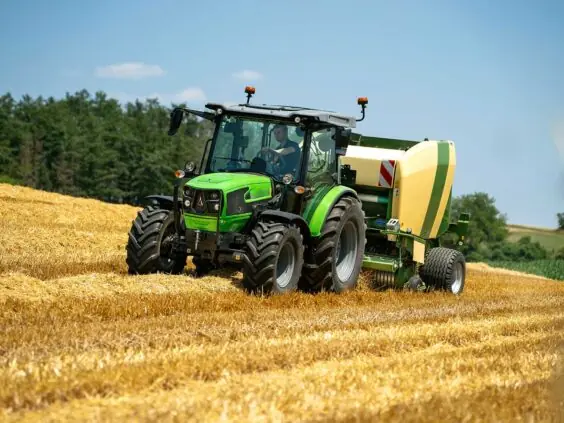 En grønn Deutz-Fahr 5D Keyline traktor som presser halm på en solfylt åker.