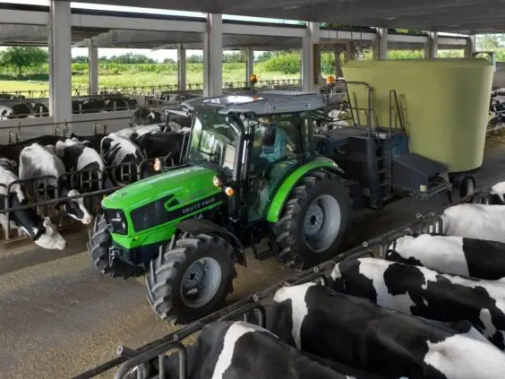 Grønn Deutz-Fahr 5D Keyline traktor som fôrer kuer i et moderne fjøs.