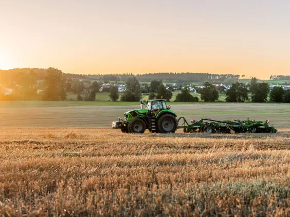En grønn Deutz-Fahr 8280 TTV traktor som arbeider på en åker i solnedgang.