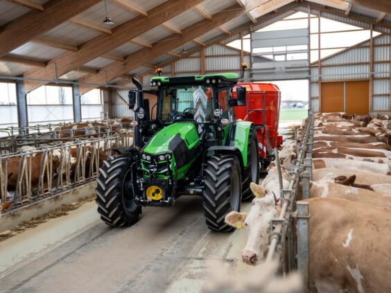 En grønn Deutz-Fahr Series 5 traktor som kjører gjennom en fjøs med kyr.
