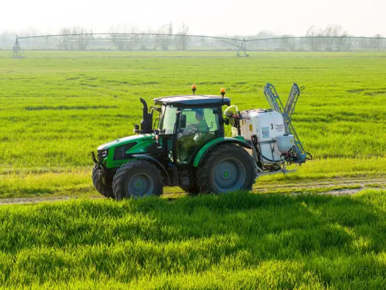 Grønn Deutz-Fahr Series 5 Keyline traktor med sprøyteutstyr i en solfylt åker.