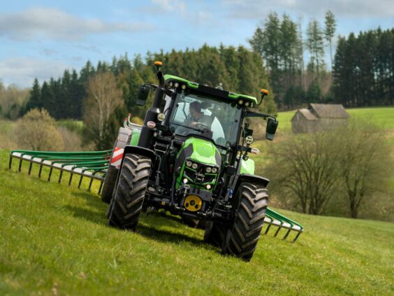 Grønn Deutz-Fahr Series 5 traktor i arbeid på en gresskledd bakke i et landskap.