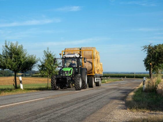 En grønn Deutz-Fahr Series 5D traktor med tilhenger full av høyballer på en vei.