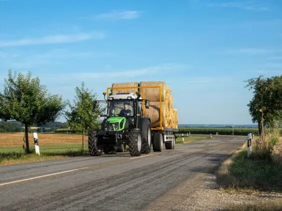 En grønn Deutz-Fahr Series 5D traktor med tilhenger full av høyballer på en vei.