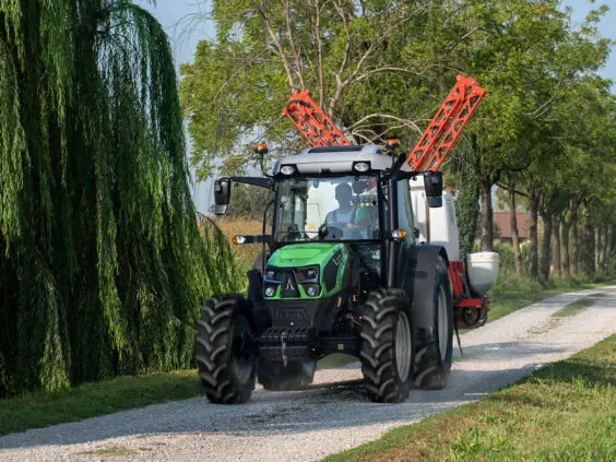 Grønn Deutz-Fahr Series 5D traktor i bevegelse på en grusvei omgitt av frodige trær.