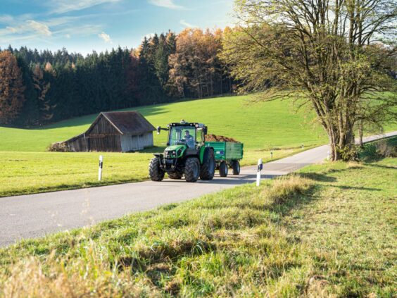 Grønn Deutz-Fahr Series 5D TTV traktor med tilhenger på en landevei i høstlandskap.
