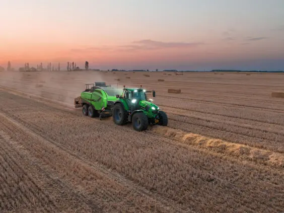 Grønn Deutz-Fahr Series 6 traktor som presser halm på en åker ved solnedgang.