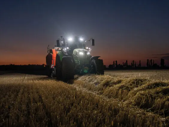 Grønn Deutz-Fahr Series 6 traktor i arbeid på kveldstid med kraftige arbeidslys tent.