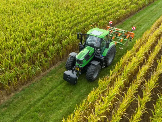 En grønn Deutz-Fahr Series 6.4 traktor i en maisåker med landbruksutstyr.