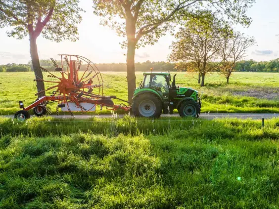 Grønn Deutz-Fahr Series 6.4 traktor med rød rive på vei i solnedgang.