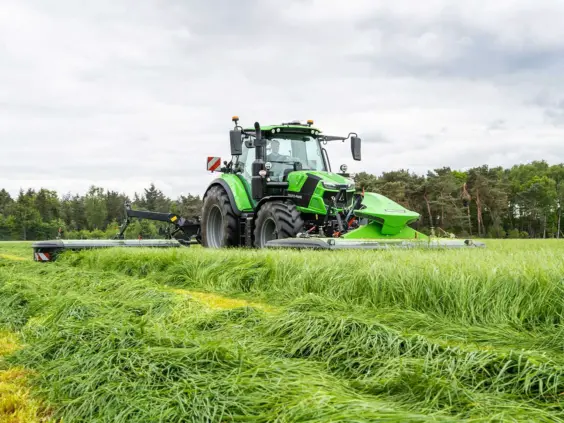En grønn Deutz-Fahr Series 6.4 traktor som slår gress på en stor, frodig eng.
