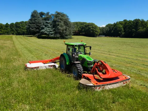 Grønn Deutz-Fahr Series 6C traktor som klipper gress på en solfylt eng.