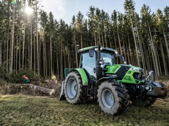 Grønn Deutz-Fahr Series 6C traktor i arbeid i skogen med skogsarbeidere.