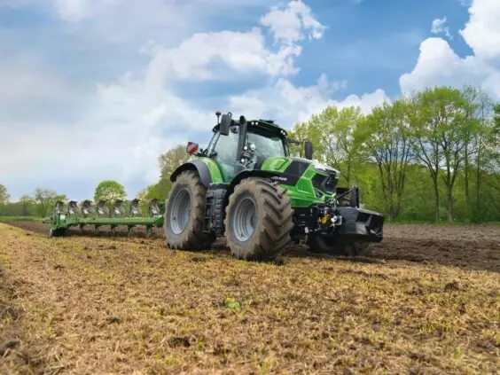 En grønn Deutz-Fahr Series 7 traktor som pløyer en åker under en blå himmel.