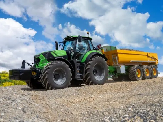En grønn Deutz-Fahr Series 7 traktor som trekker en stor gul tilhenger på grus.