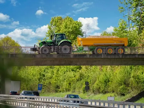 En Deutz-Fahr Series 7 traktor med gul tilhenger på en bro over en motorvei.