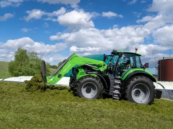 Deutz-Fahr Series 7 traktor med frontlaster i arbeid på en stor gresshaug ute.