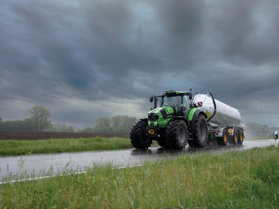 En grønn Deutz-Fahr Series 7 traktor kjører på en våt vei med en stor tankvogn.
