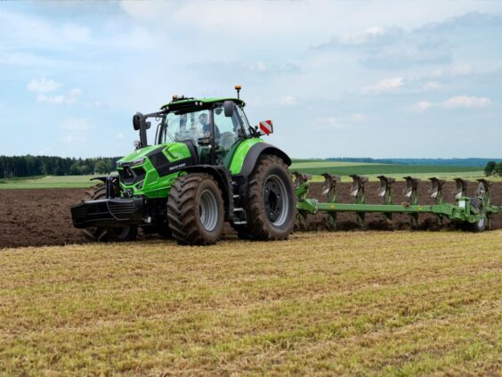 En grønn Deutz-Fahr Series 7 traktor som pløyer en åker under en blå himmel.