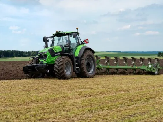 En grønn Deutz-Fahr Series 7 traktor som pløyer en åker under en blå himmel.