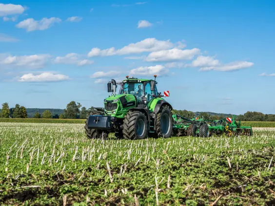 Grønn Deutz-Fahr Series 8 traktor i arbeid på en åker under blå himmel.