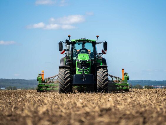 Grønn Deutz-Fahr Series 8 traktor i arbeid på en åpen åker under blå himmel.
