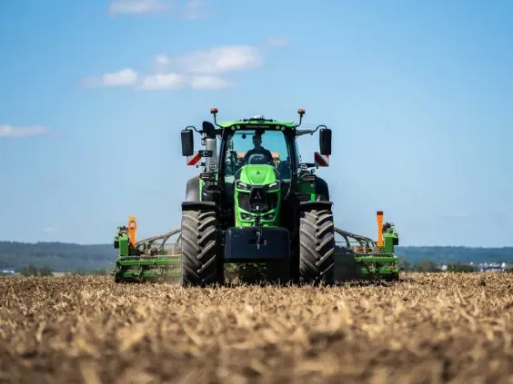 Grønn Deutz-Fahr Series 8 traktor i arbeid på en åpen åker under blå himmel.