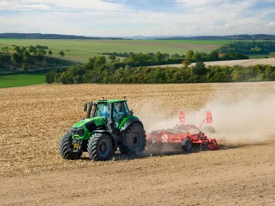 Grønn Deutz-Fahr Series 9 traktor i arbeid på en tørr åker under blå himmel.