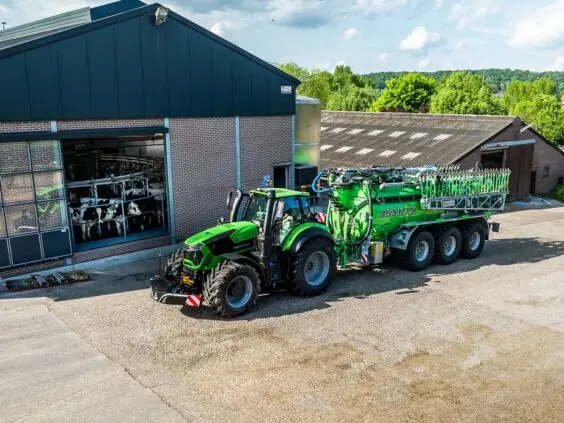 Grønn Deutz-Fahr Series 9 traktor med Joskin tankvogn foran en fjøs på en gård.