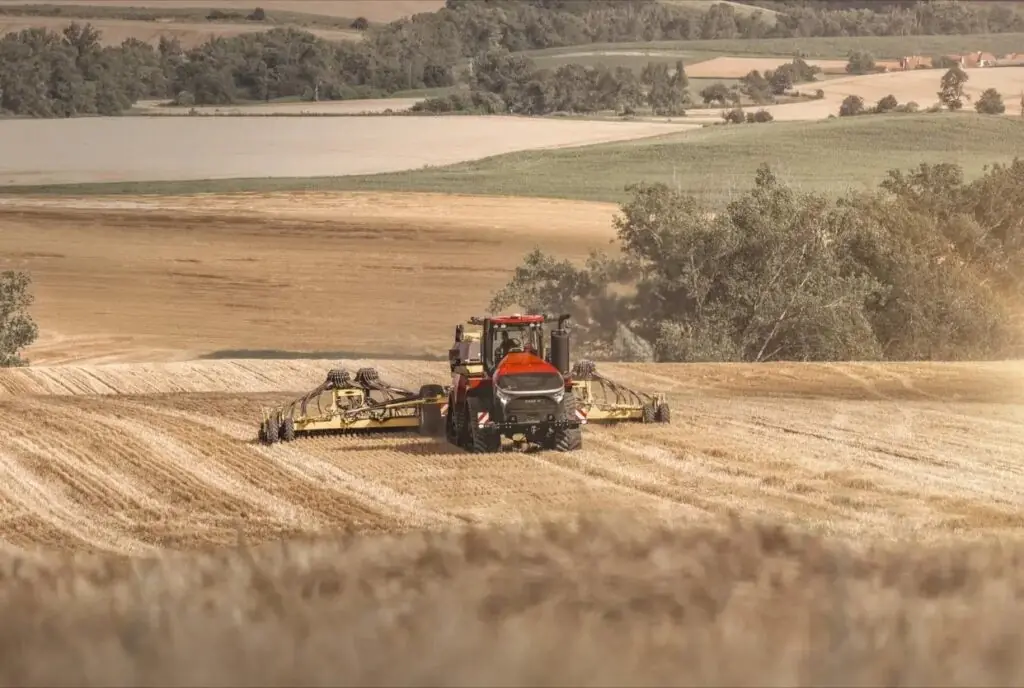 En rød Steiger 785 Quadtrac traktor som jobber på en gyllen åker under innhøsting.