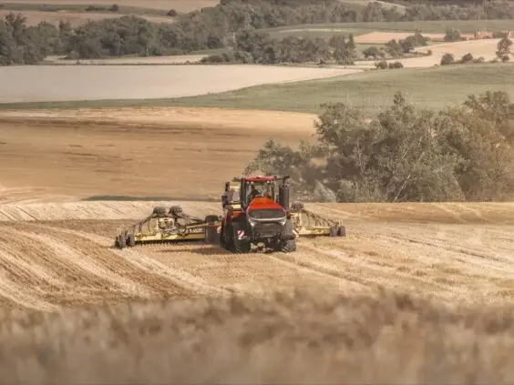 En rød Steiger 785 Quadtrac traktor som jobber på en gyllen åker under innhøsting.
