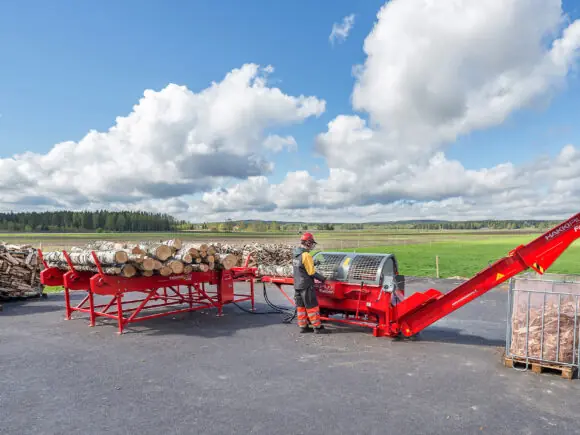 En operatør som bruker en rød Hakki Pilke Falcon 37 vedmaskin utendørs.