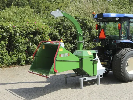 Grønn NHS 150i flishugger montert bak på en blå traktor utendørs.