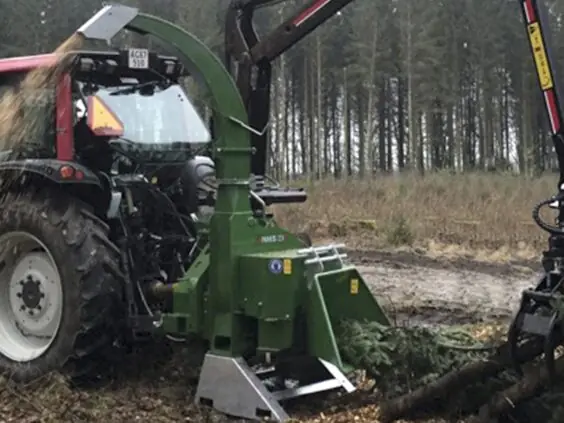 En rød traktor i skogen med en grønn NHS 220ic flishugger i arbeid.