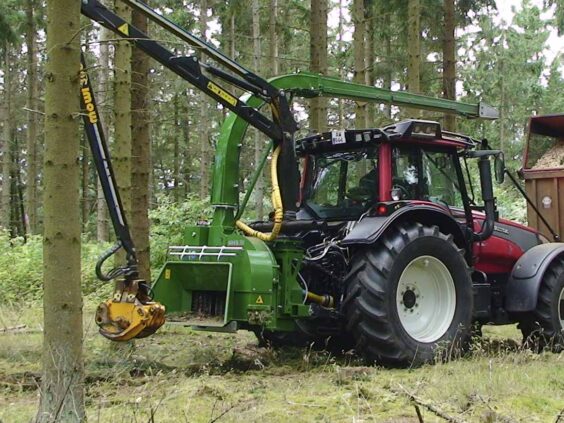 En grønn NHS 300f flishugger montert på en rød traktor i skogen under arbeid.