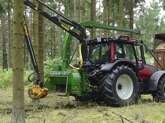 En grønn NHS 300f flishugger montert på en rød traktor i skogen under arbeid.