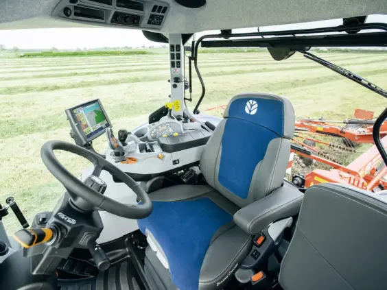 Interiør av en moderne T7 SWB traktor med kontrollpanel og utsikt over en åker.