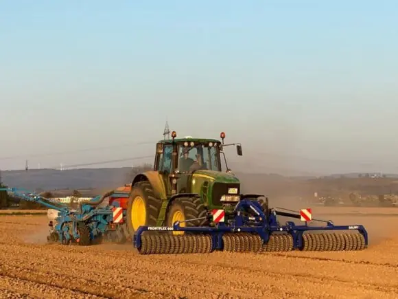 En traktor i feltet utstyrt med en blå DALBO Frontflex frontmontert trommel.